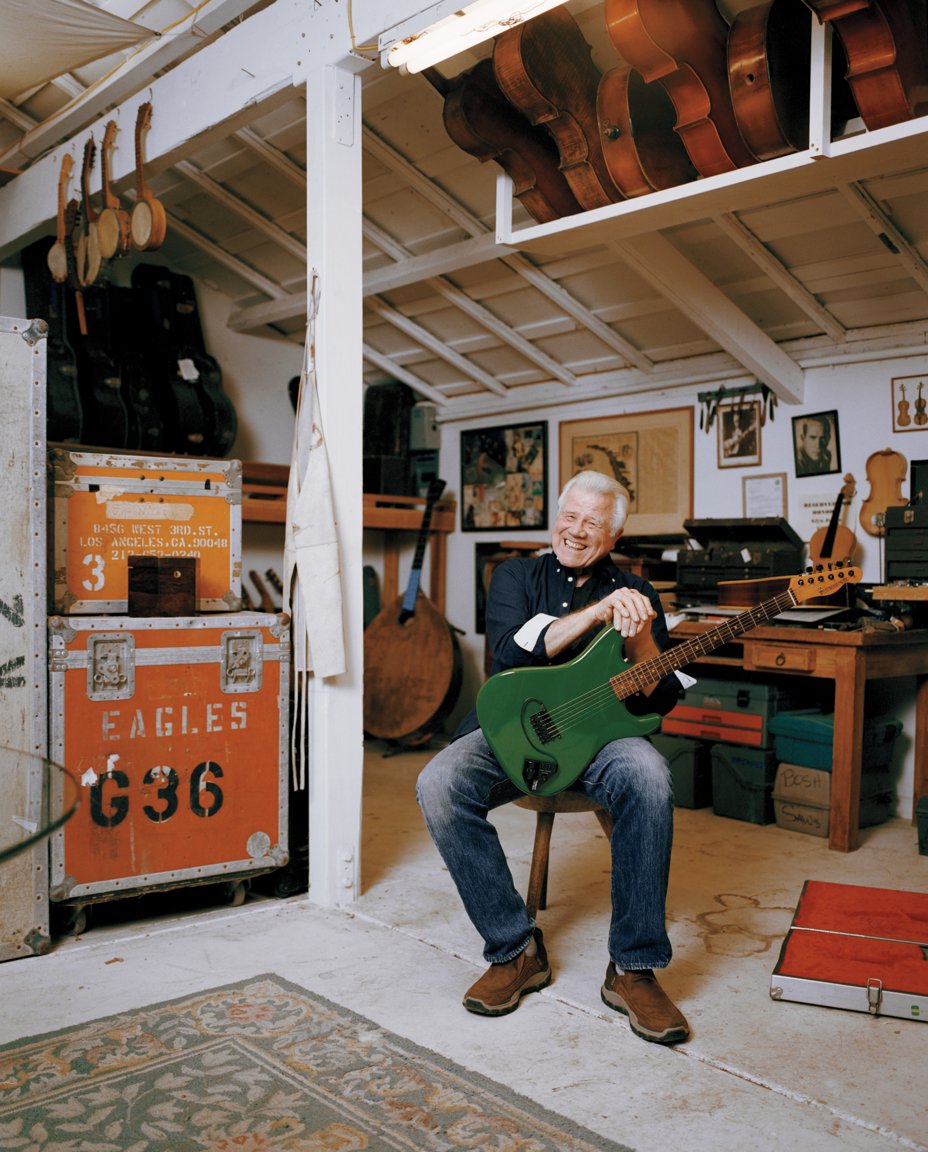 photo of grinning man sitting in airy lofted studio with green guitar on his lap, surrounded by musical instruments and equipment