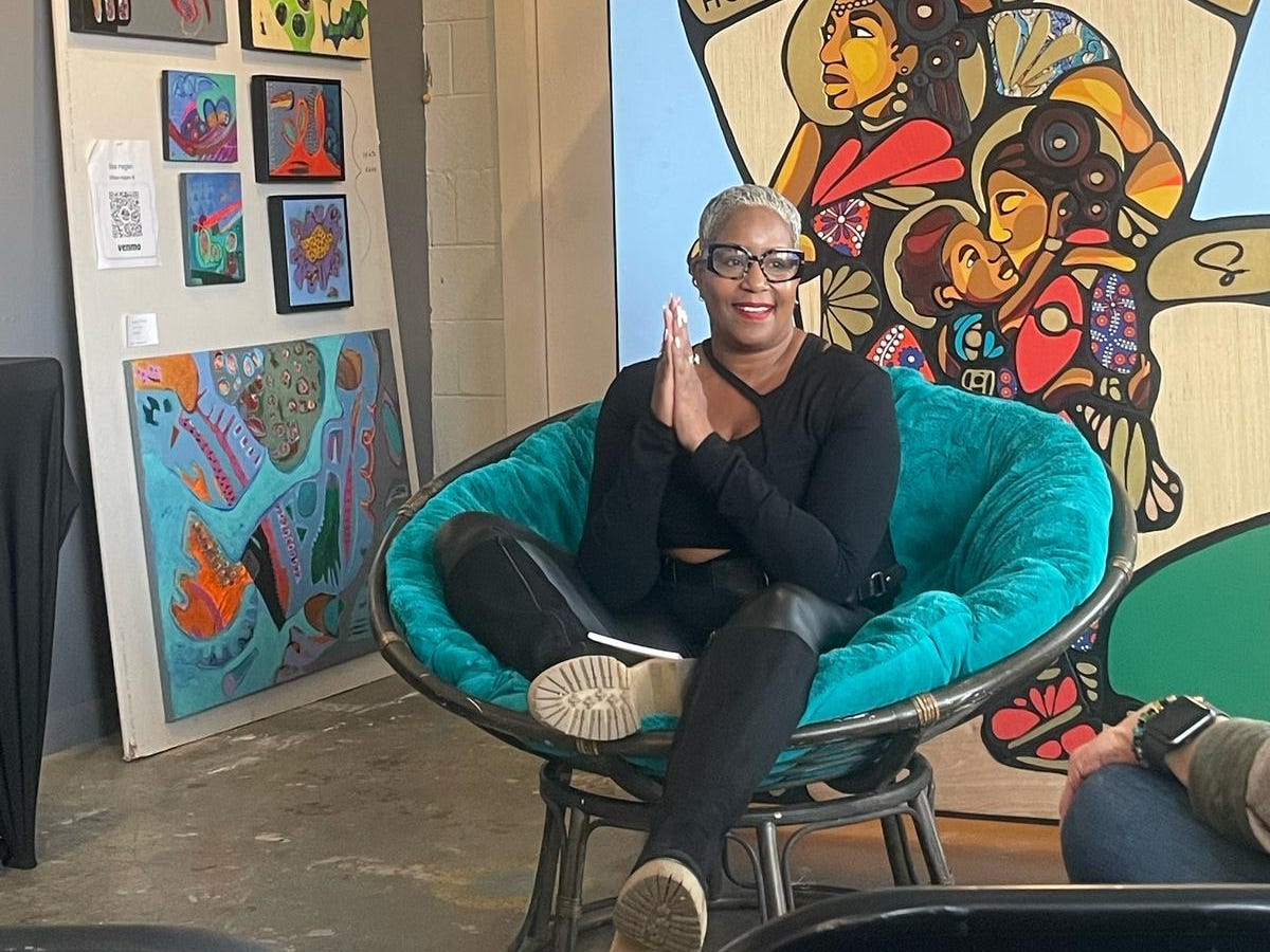 Samantha sits on a round chair in front of different pieces of art.