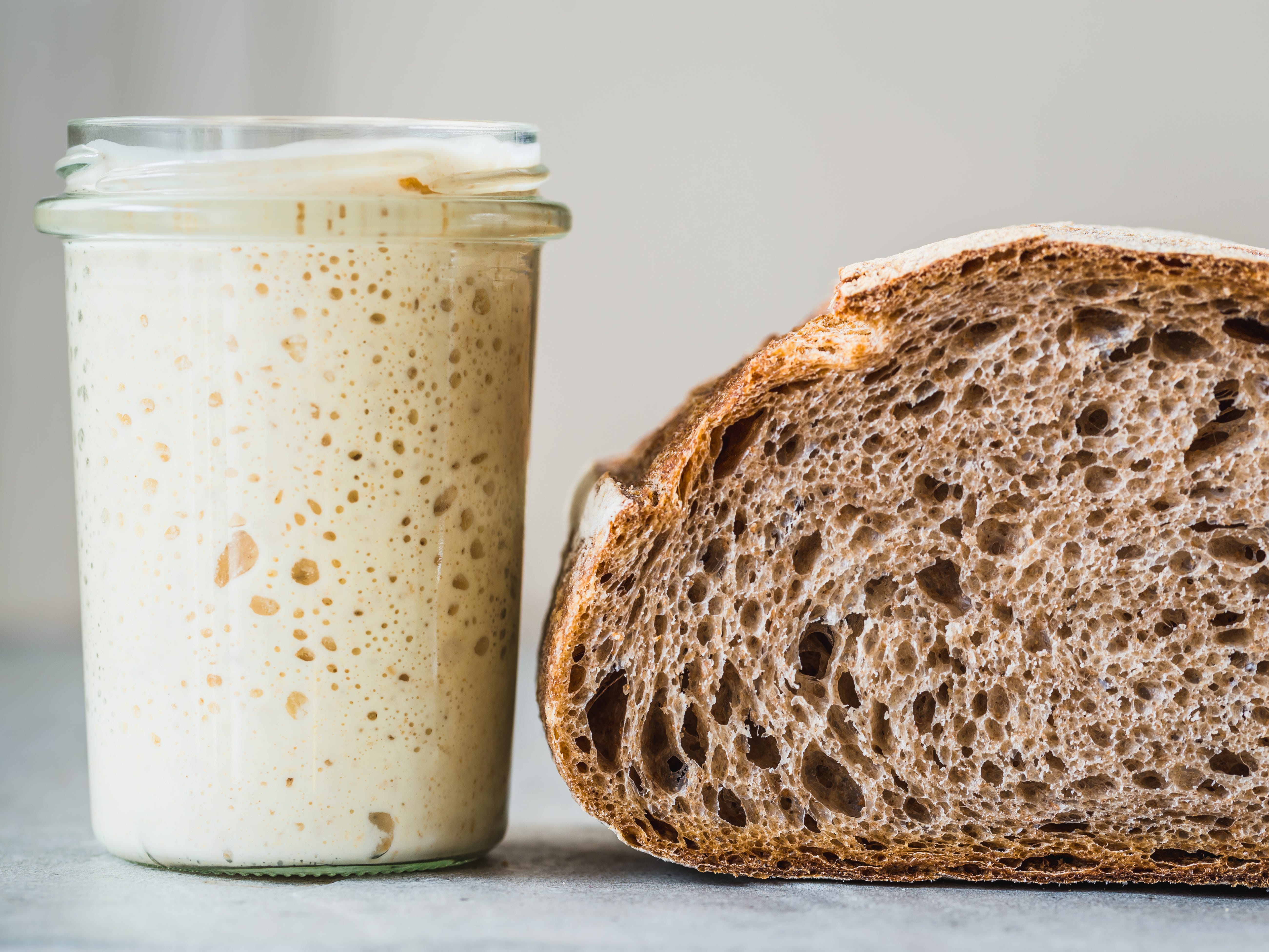 A jar of sourdough starter next to a loaf of the baked bread.