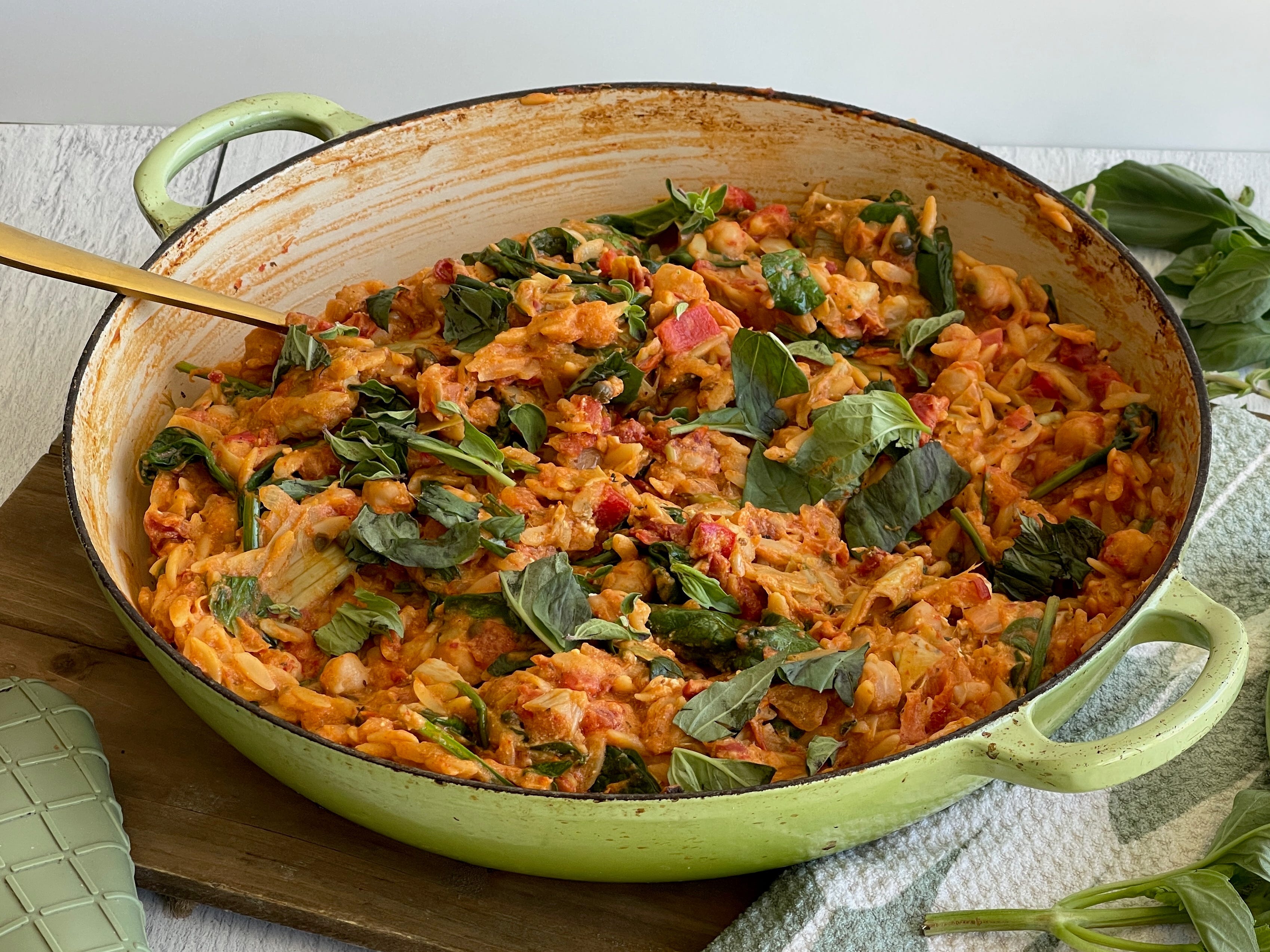 Cooked orzo in a pan garnished with basil leaves on a kitchen table.
