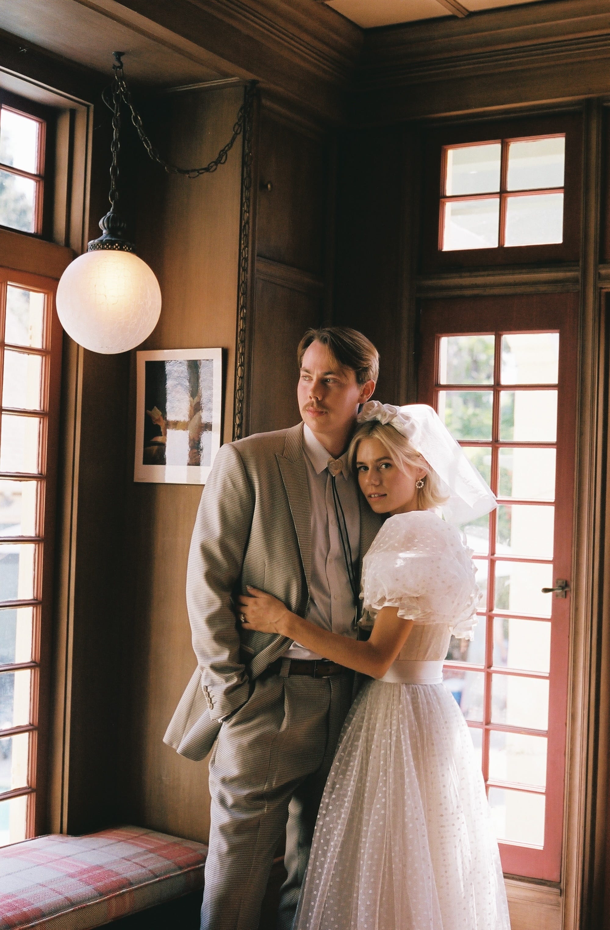 A bride and groom embrace in a room with glass doors.