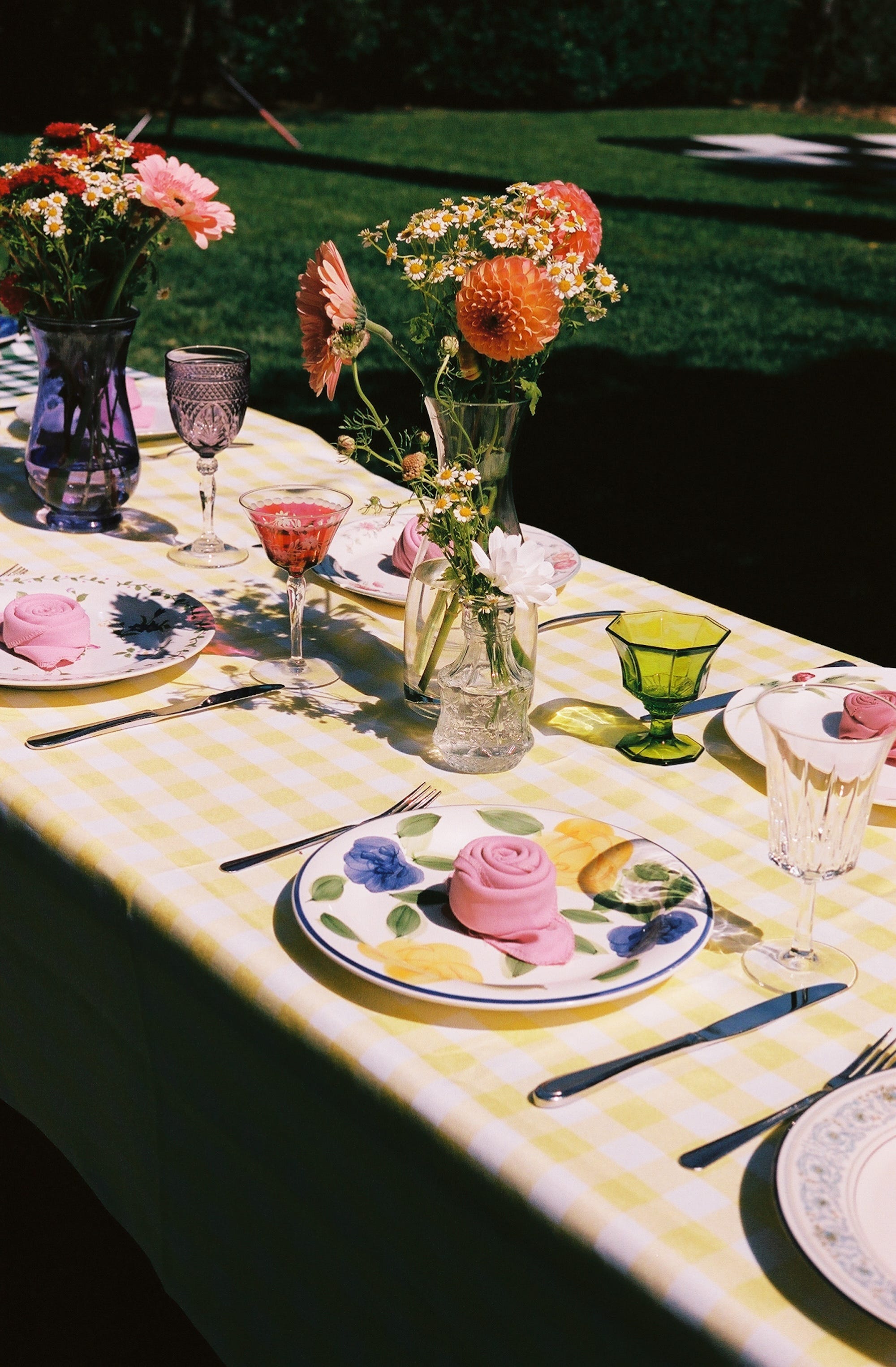 A table with gingham tablecloths, mismatched plates, and colorful flowers.