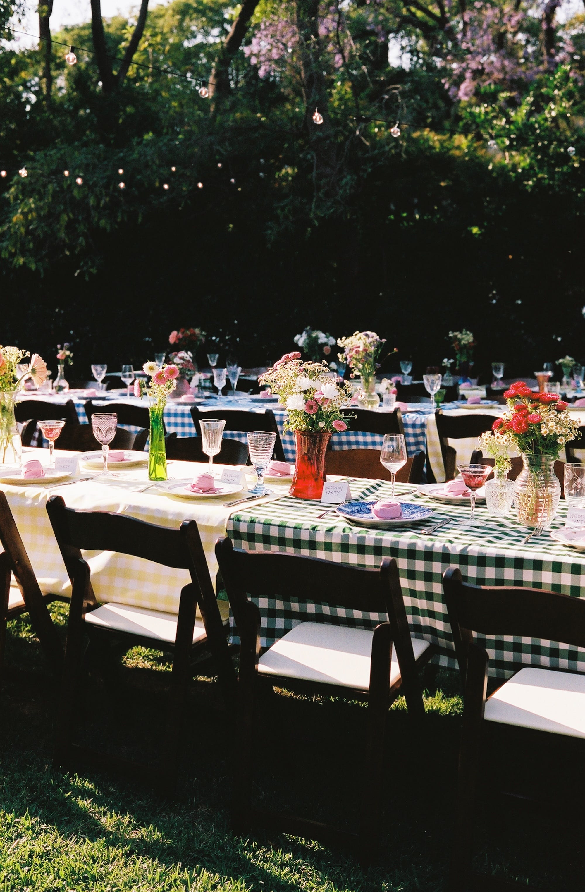 Multiple tables with gingham tablecloths and displays of flowers.