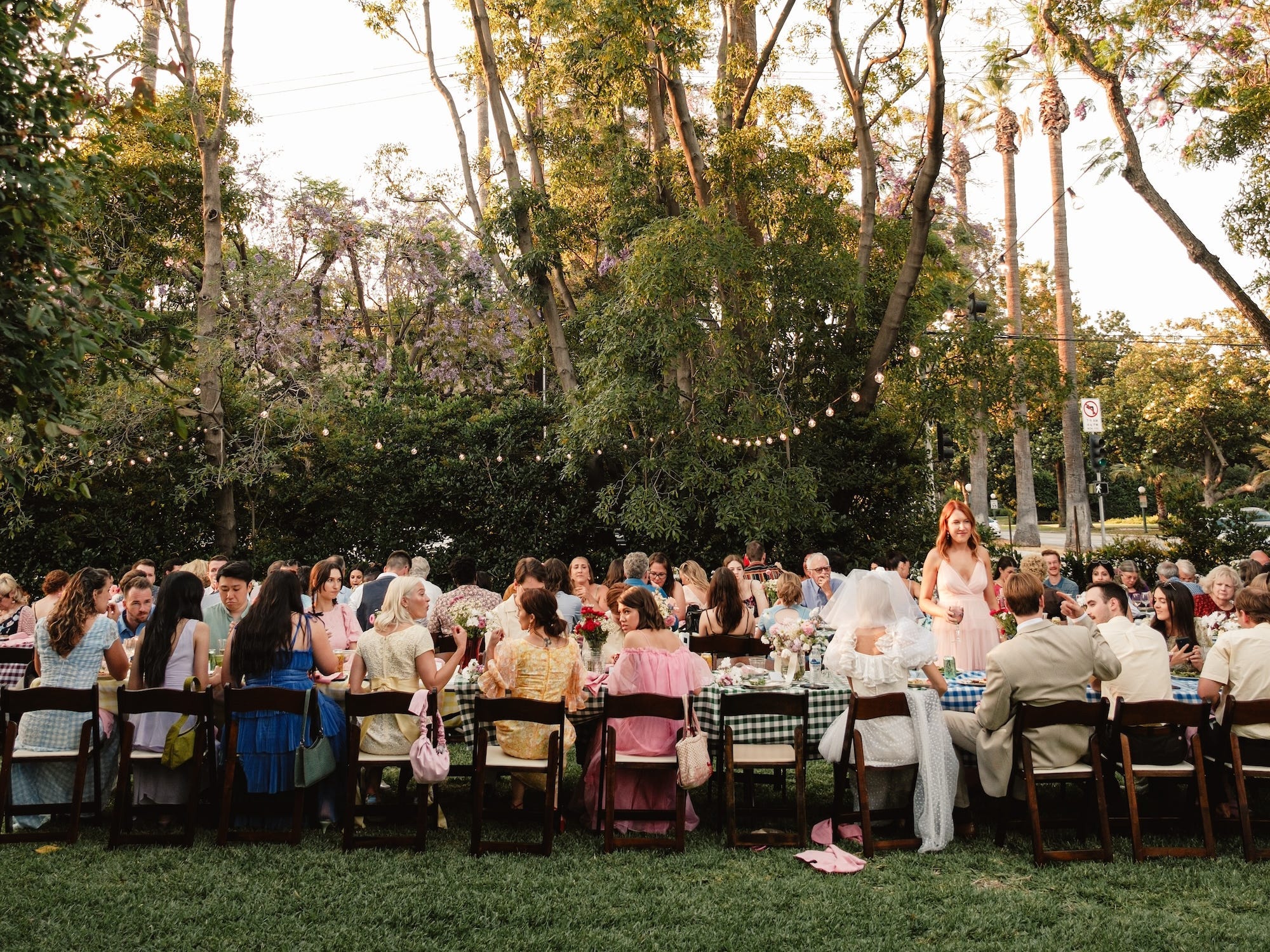 A wide shot of a couple's wedding reception. Guests sit at long tables, chatting.