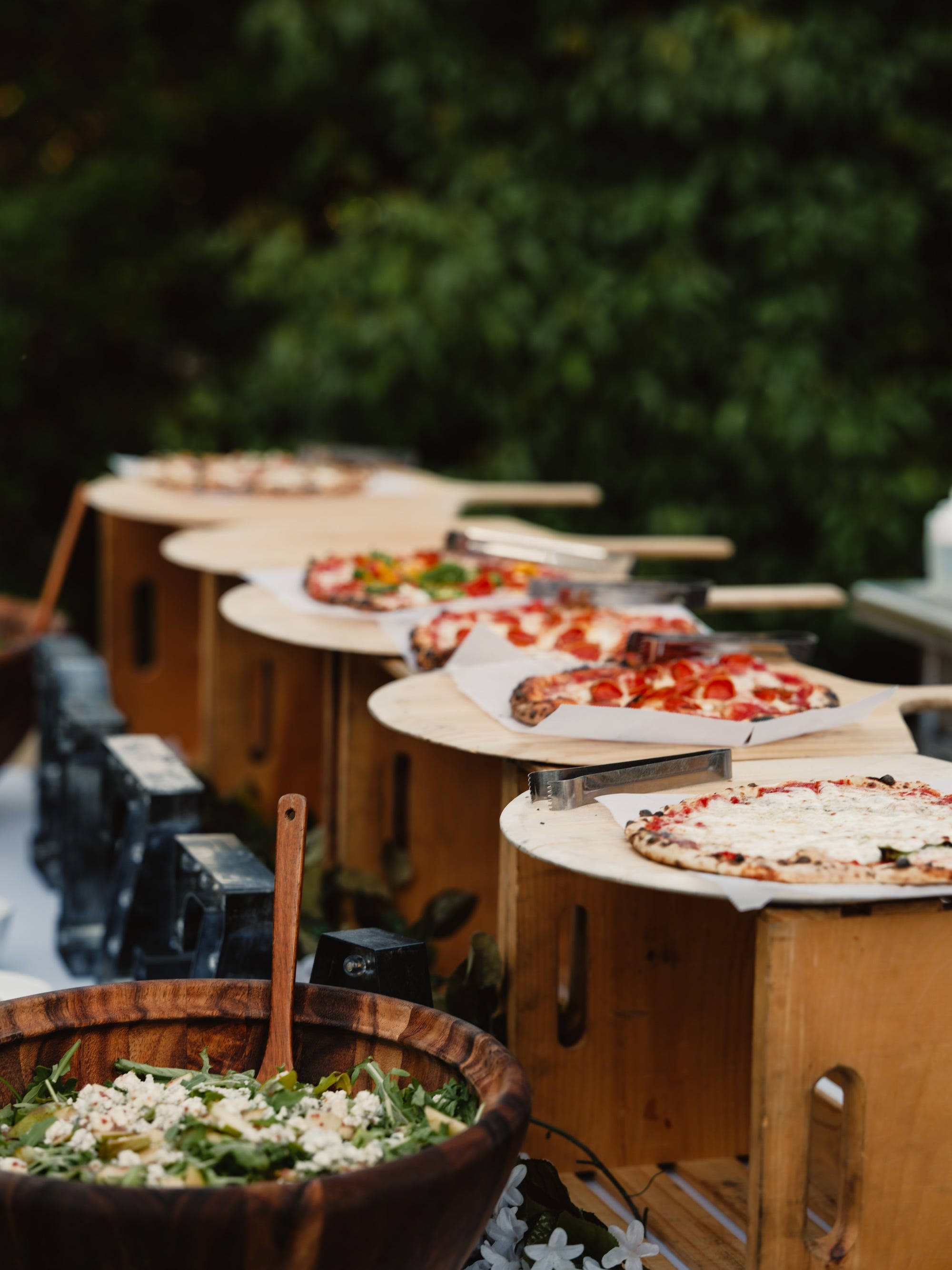 A table with multiple pizzas and a salad bowl on it.