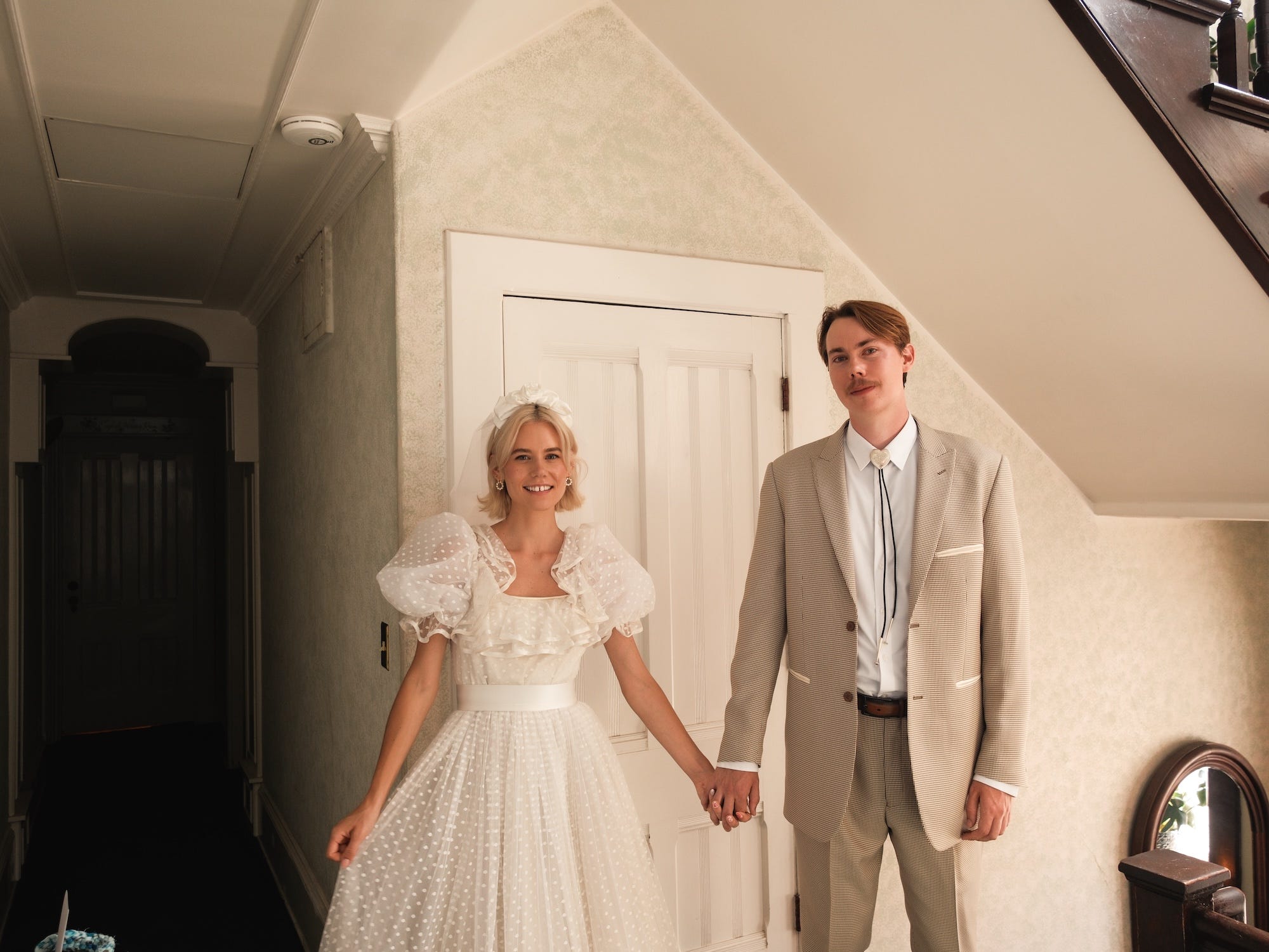 A bride and groom hold hands in a house.