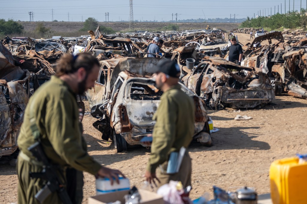 Workers searching through burned-out cars in Tkuma, Israel.