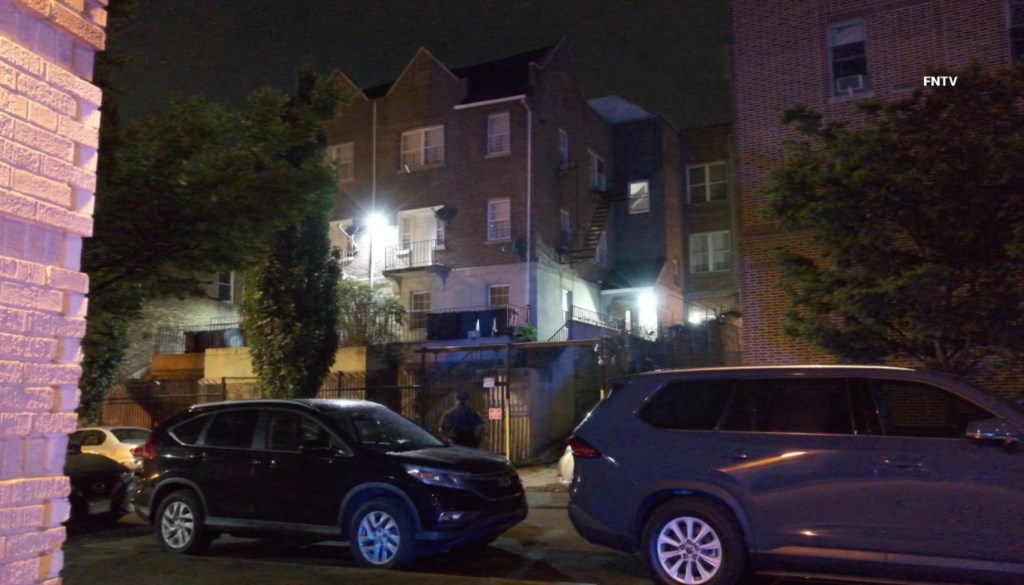 Nighttime photo of a brick apartment building with cars parked in front.