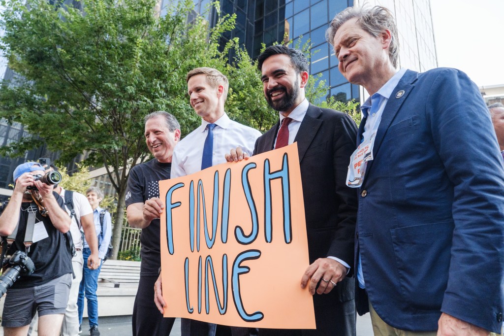 Zohran Mamdani and other politicians at a finish line holding a sign.