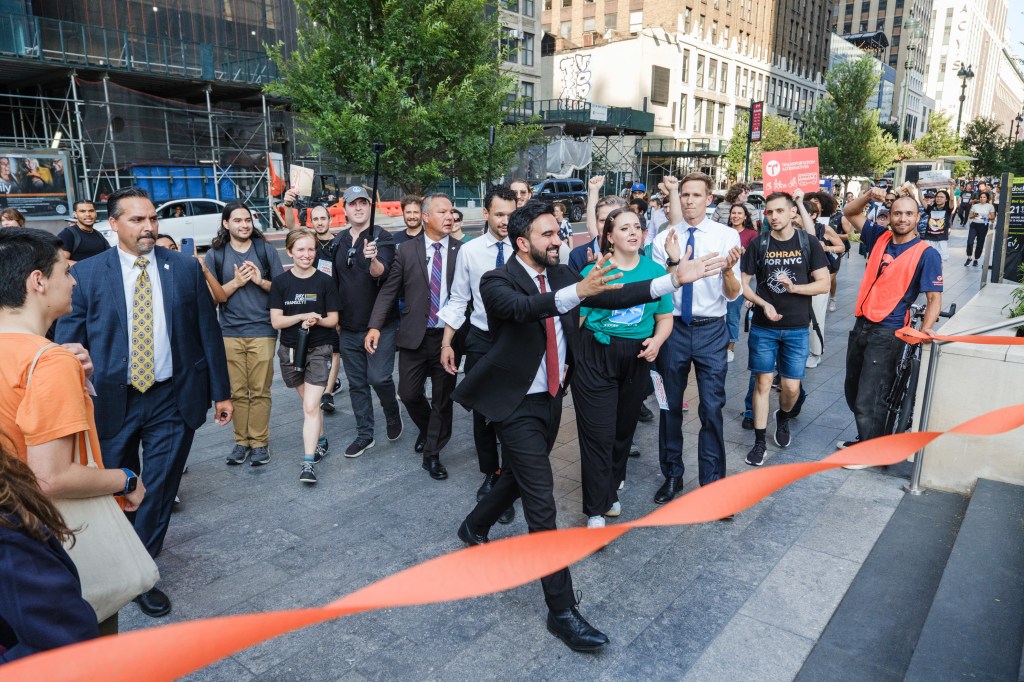 NYC mayoral candidate Zohran Mamdani racing on foot against a bus.