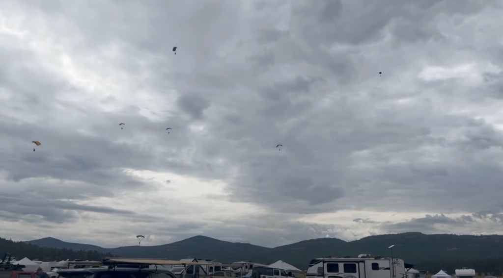 Several parachutists descending under cloudy skies.