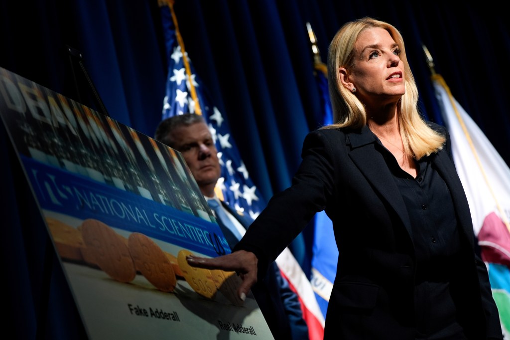 Attorney General Pam Bondi pointing to a graphic comparing real and fake Adderall pills at a DEA press conference.