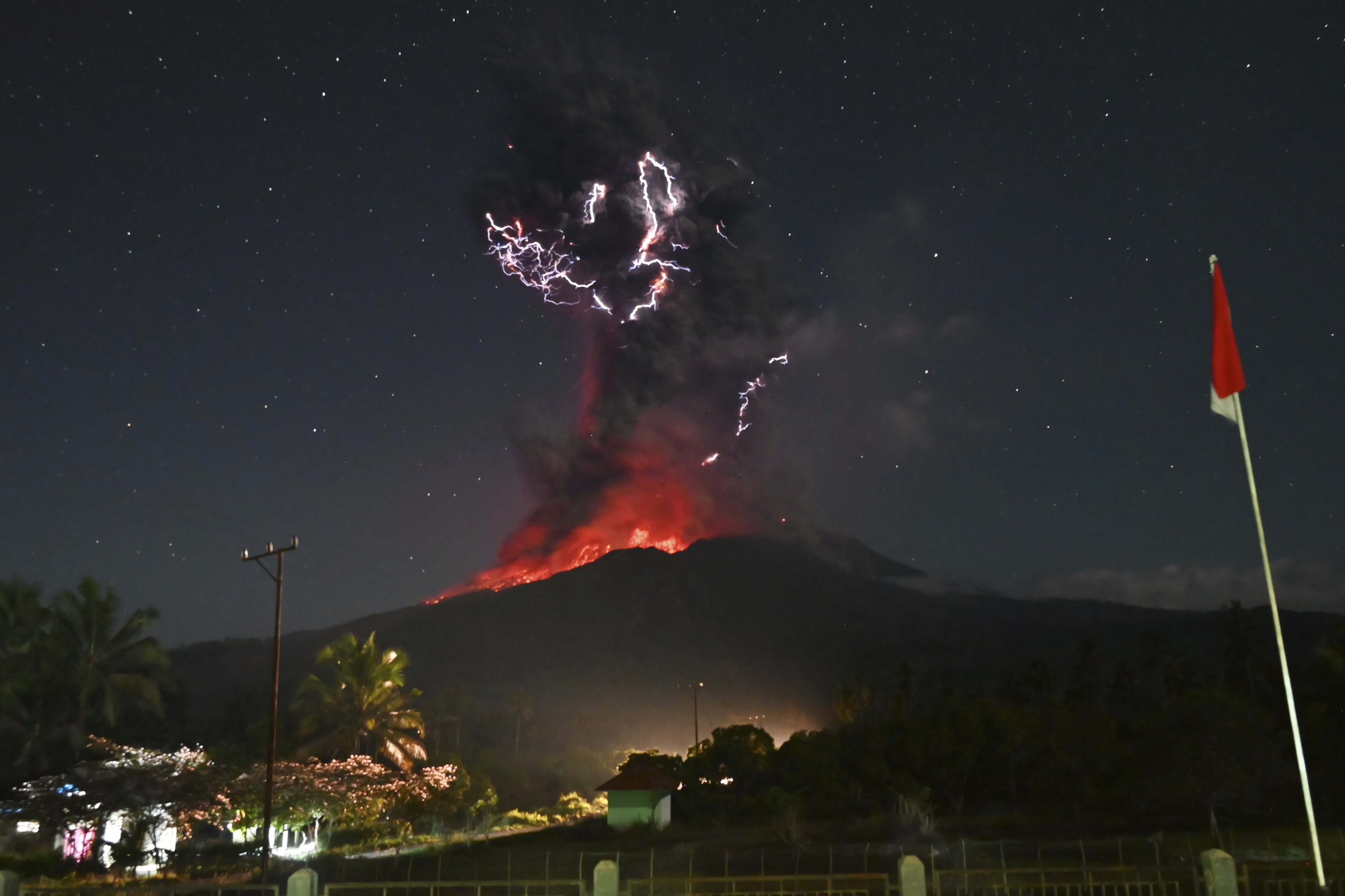 Many bolts of lightning flash inside a volcanic ash cloud above an erupting volcano at night.