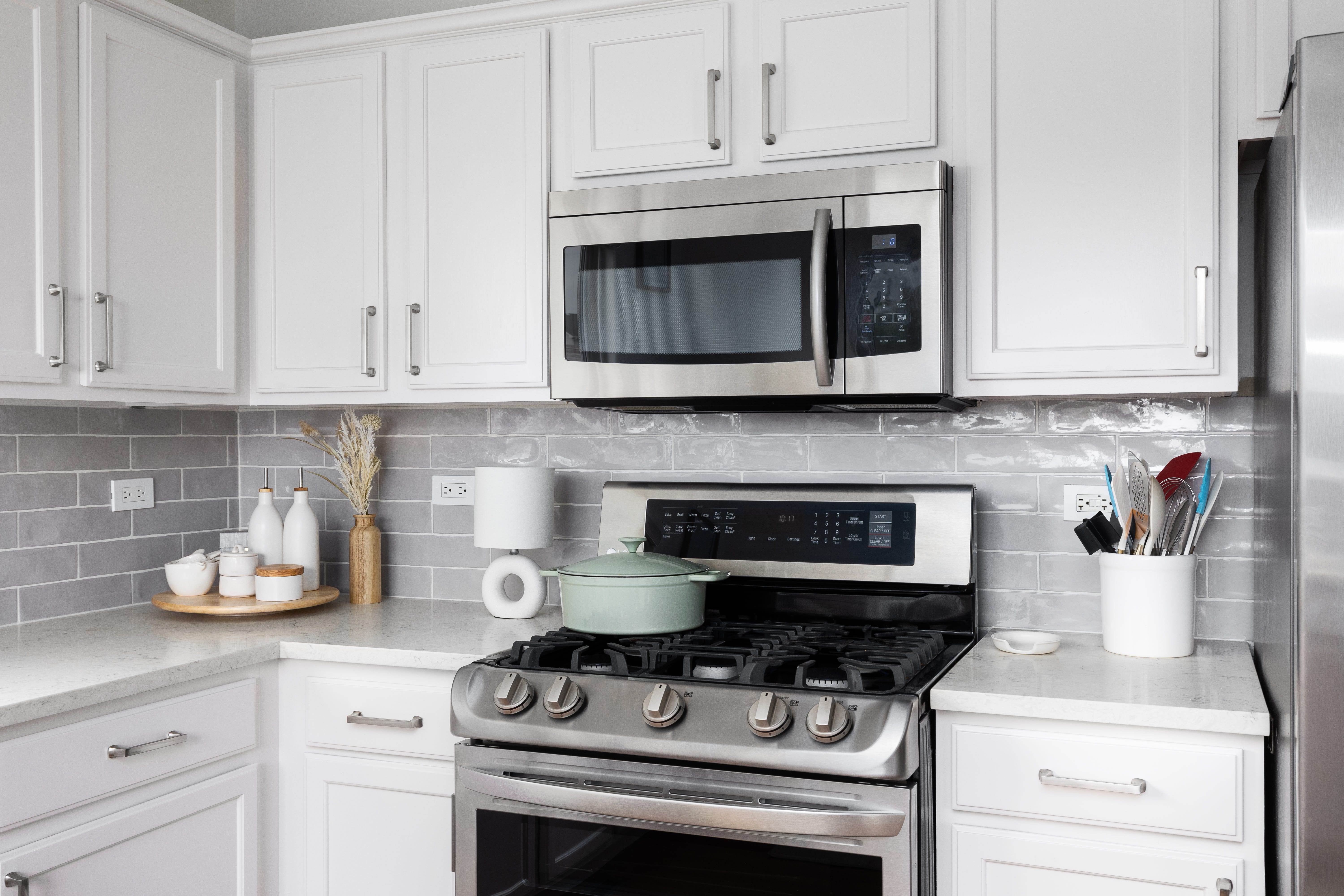 White kitchen with gray backplash, stainless steel oven and microwave