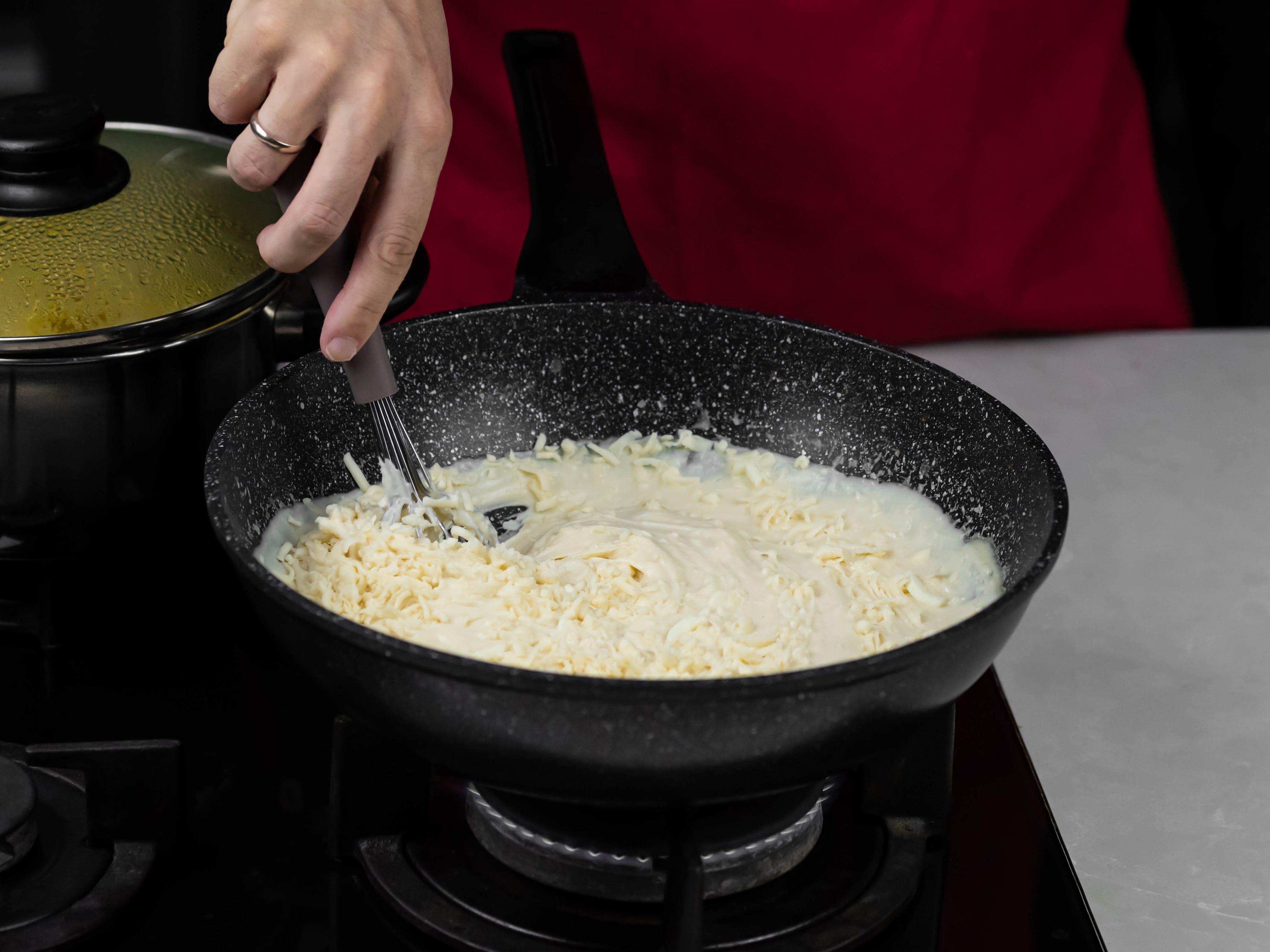 Person stirring cheese into pan of mac and cheese sauce on black stove