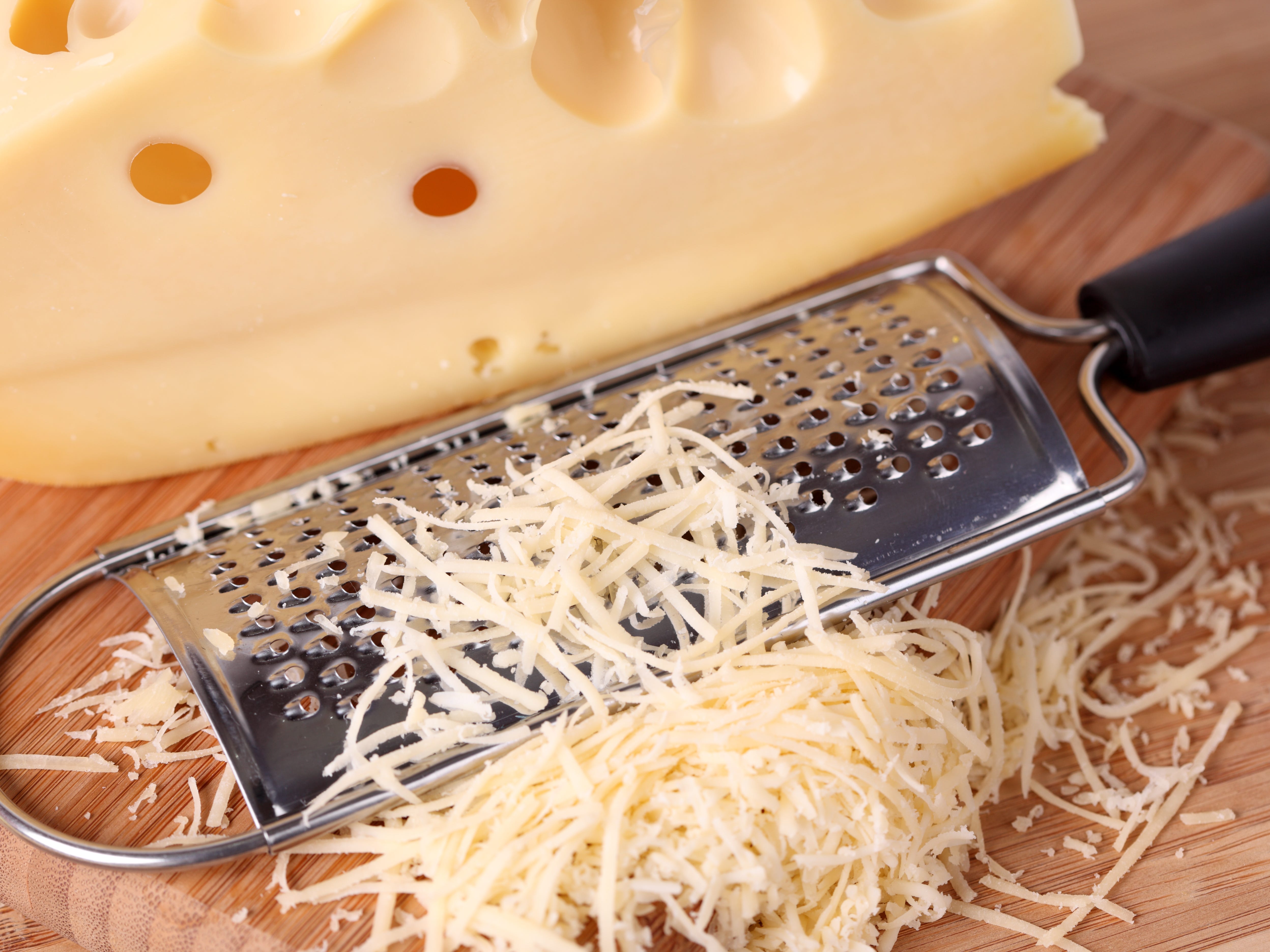 block of cheese beside pile of grated cheese and metal grater