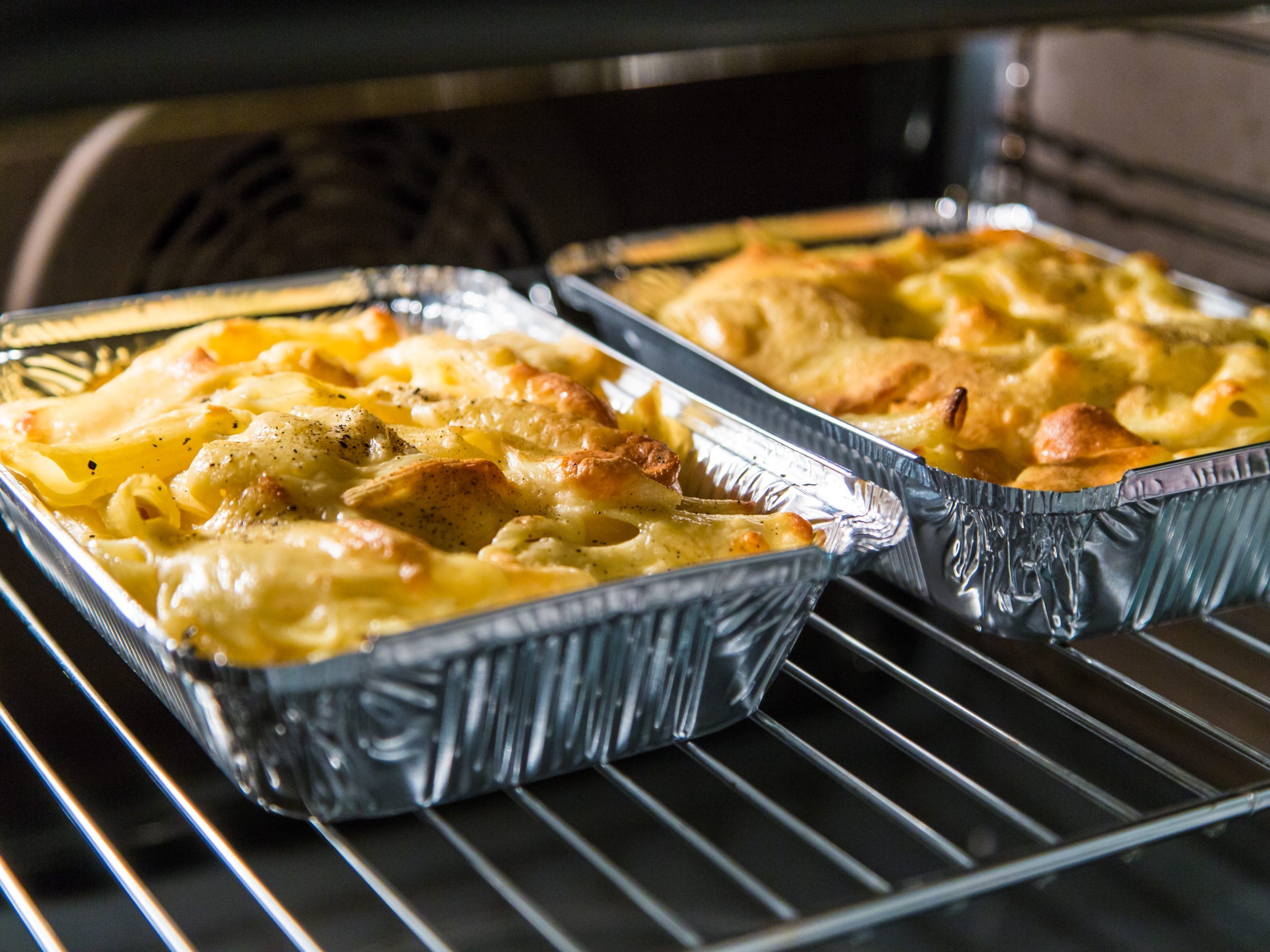 Two metal trays of mac and cheese baking on rack in oven