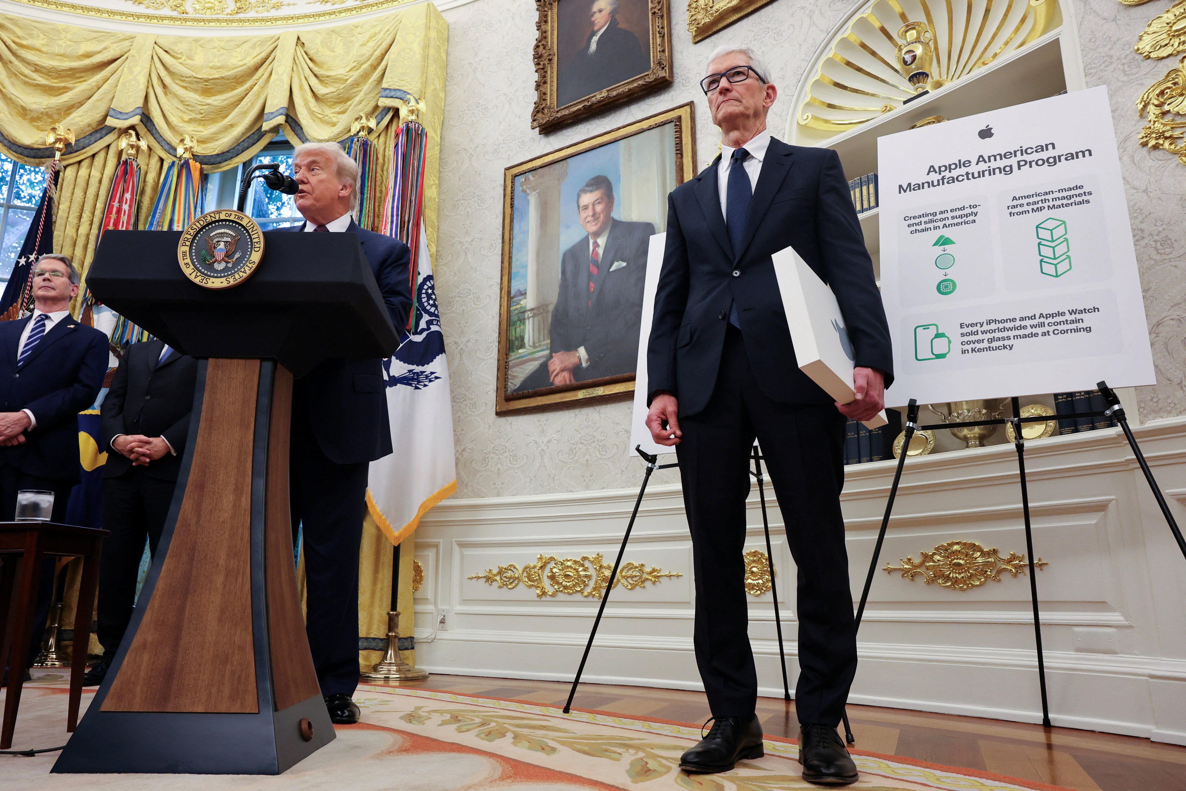 US President Donald Trump speaks as Apple CEO Tim Cook stands, as they present Apple's announcement of a $100 billion investment in U.S. manufacturing, in the Oval Office at the White House in Washington, D.C., U.S., August 6, 2025.