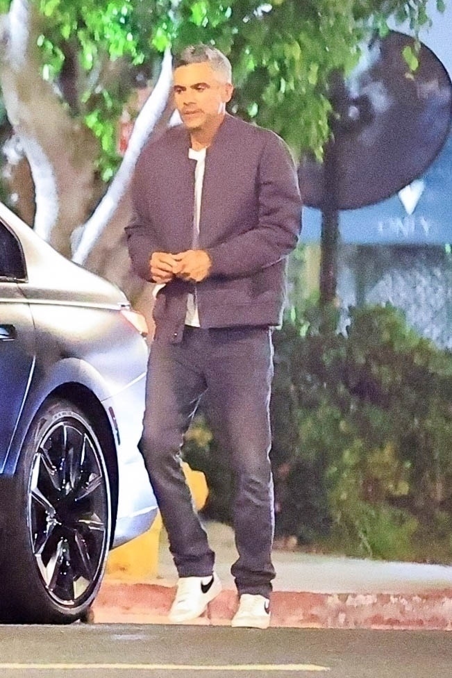 Cash Warren in a dark jacket next to a BMW at night. 