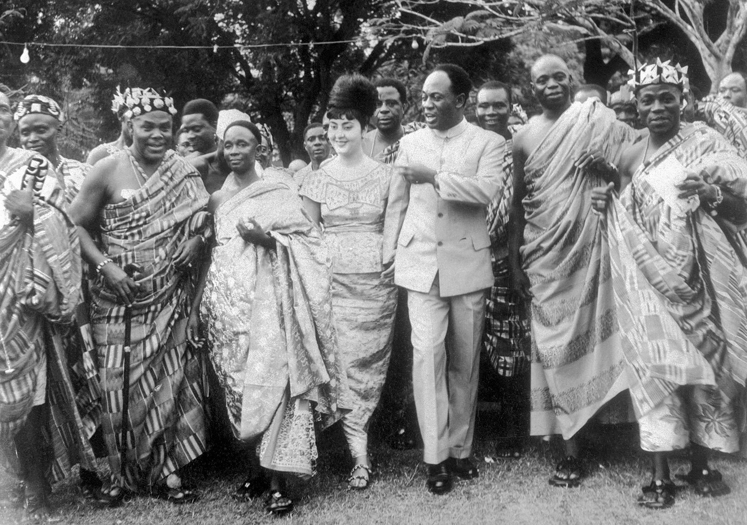 A man in a suit and woman in a dress are surrounded by people in long robes smiling and dancing.
