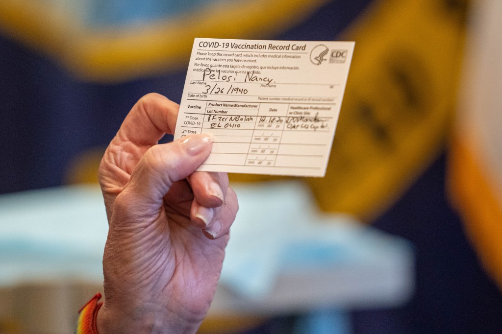 Close-up of Nancy Pelosi's hand holding her COVID-19 vaccination record card.