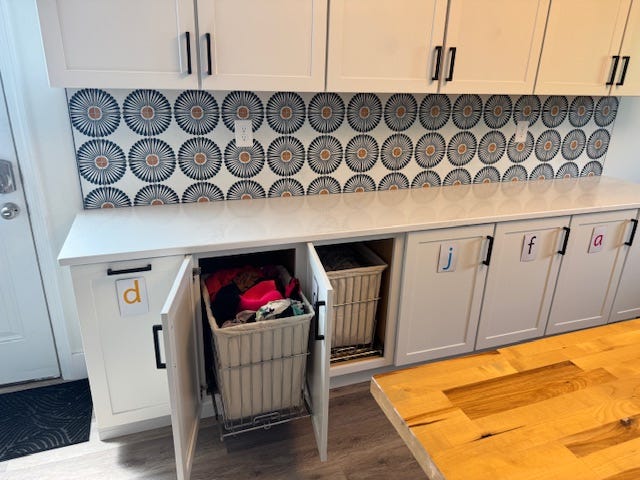 Cabinets with pull-out laundry baskets labeled with the initials of the author's family members.