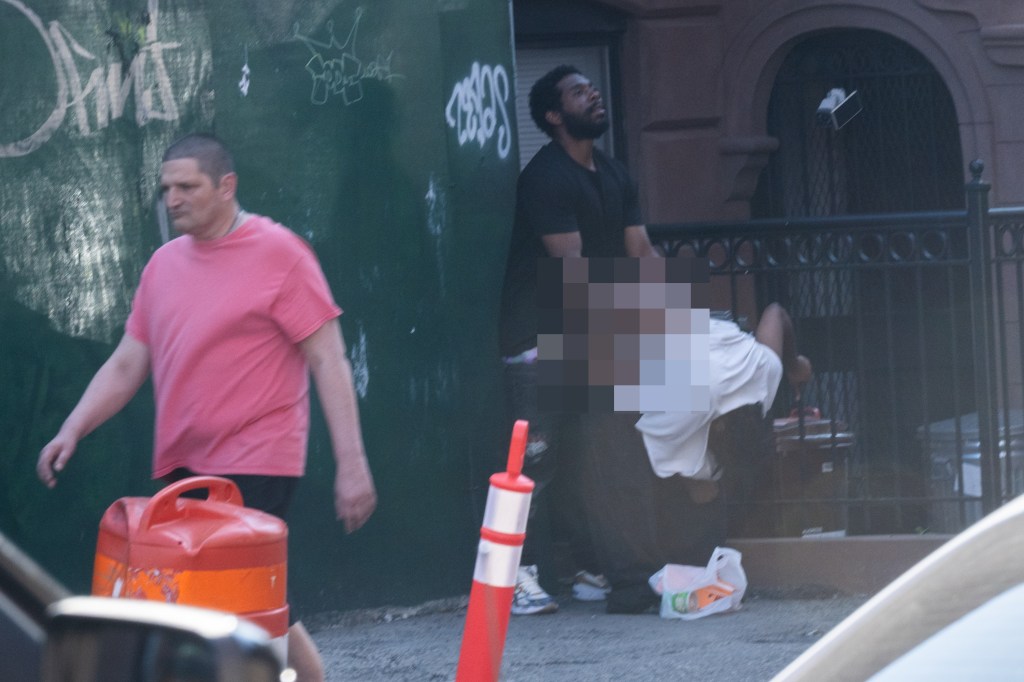 A person in a pink shirt walks past two people near a fence; one person's torso is obscured.