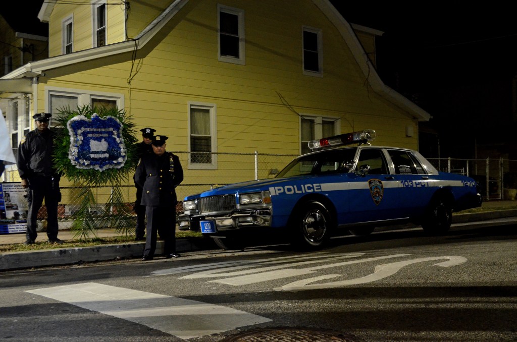 NYPD officers at a vigil with a wreath and vintage police car.