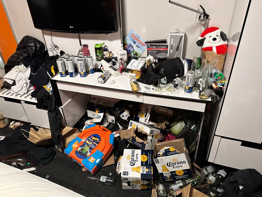 Messy hotel room with discarded belongings and numerous empty Corona beer cans and bottles.