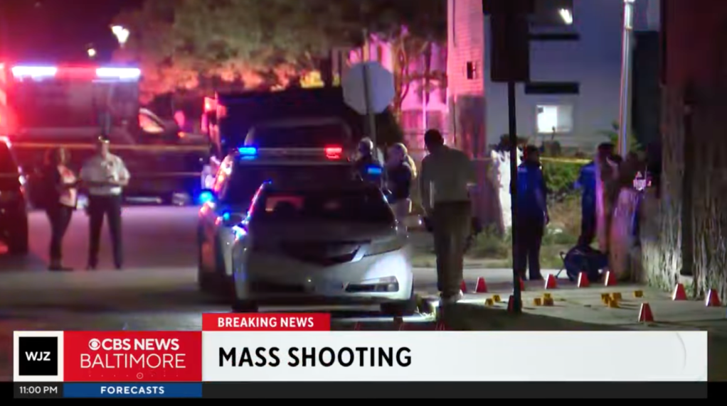 Law enforcement officials investigate the shooting on the sidewalk of the street.