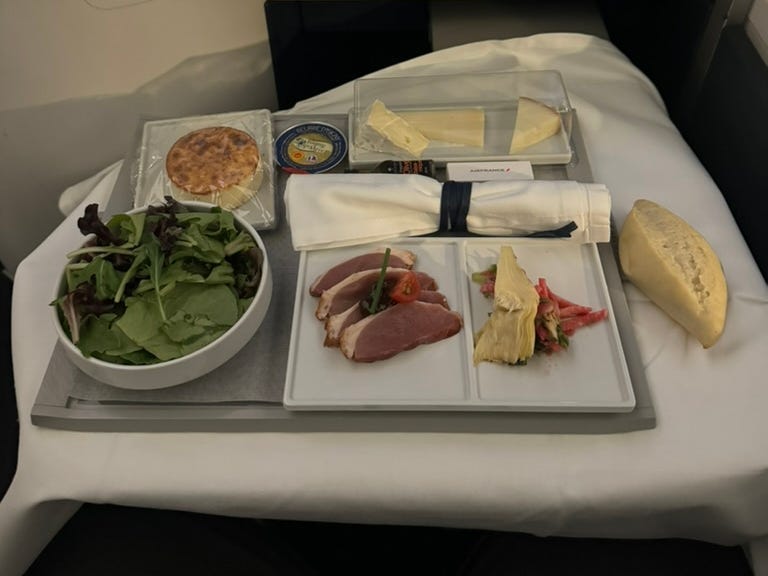 Tray of food with salad, cheesecake, bread, and other food items on tray on plane