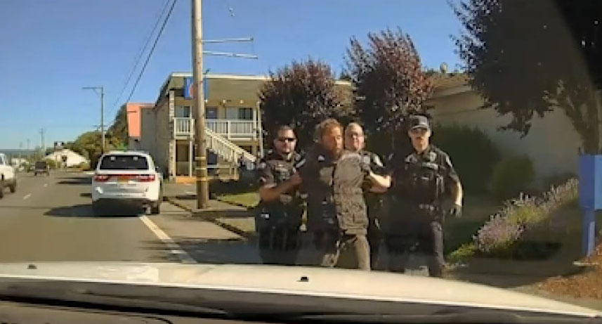 Man in handcuffs escorted by police officers.