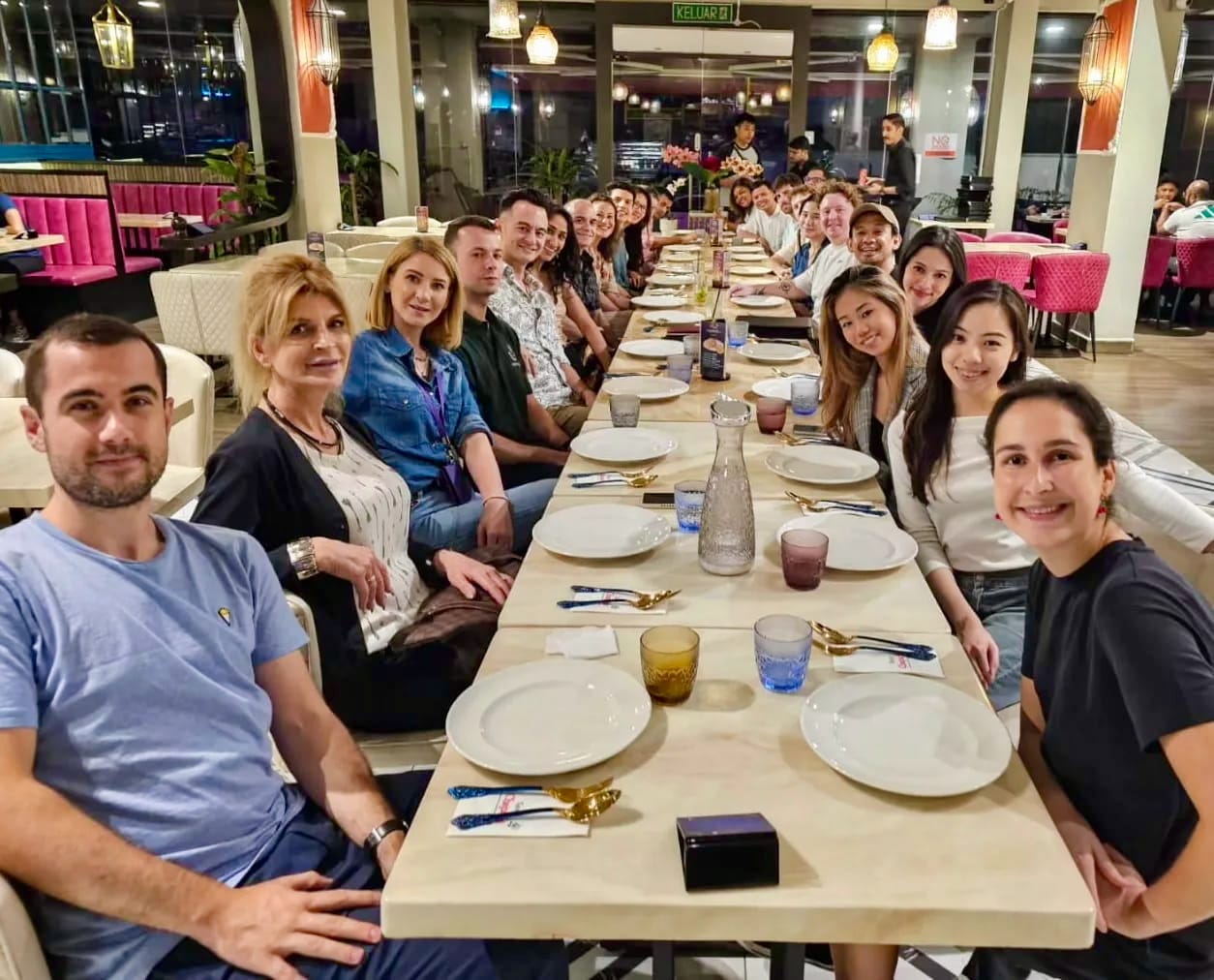 A group of people seated along a long table during an expat club meetup in Malaysia.