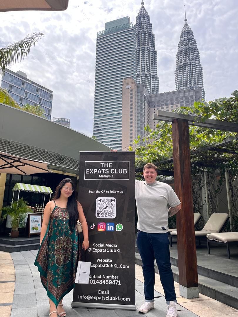 A couple posing with a banner for the Expats Club KL in Malaysia.