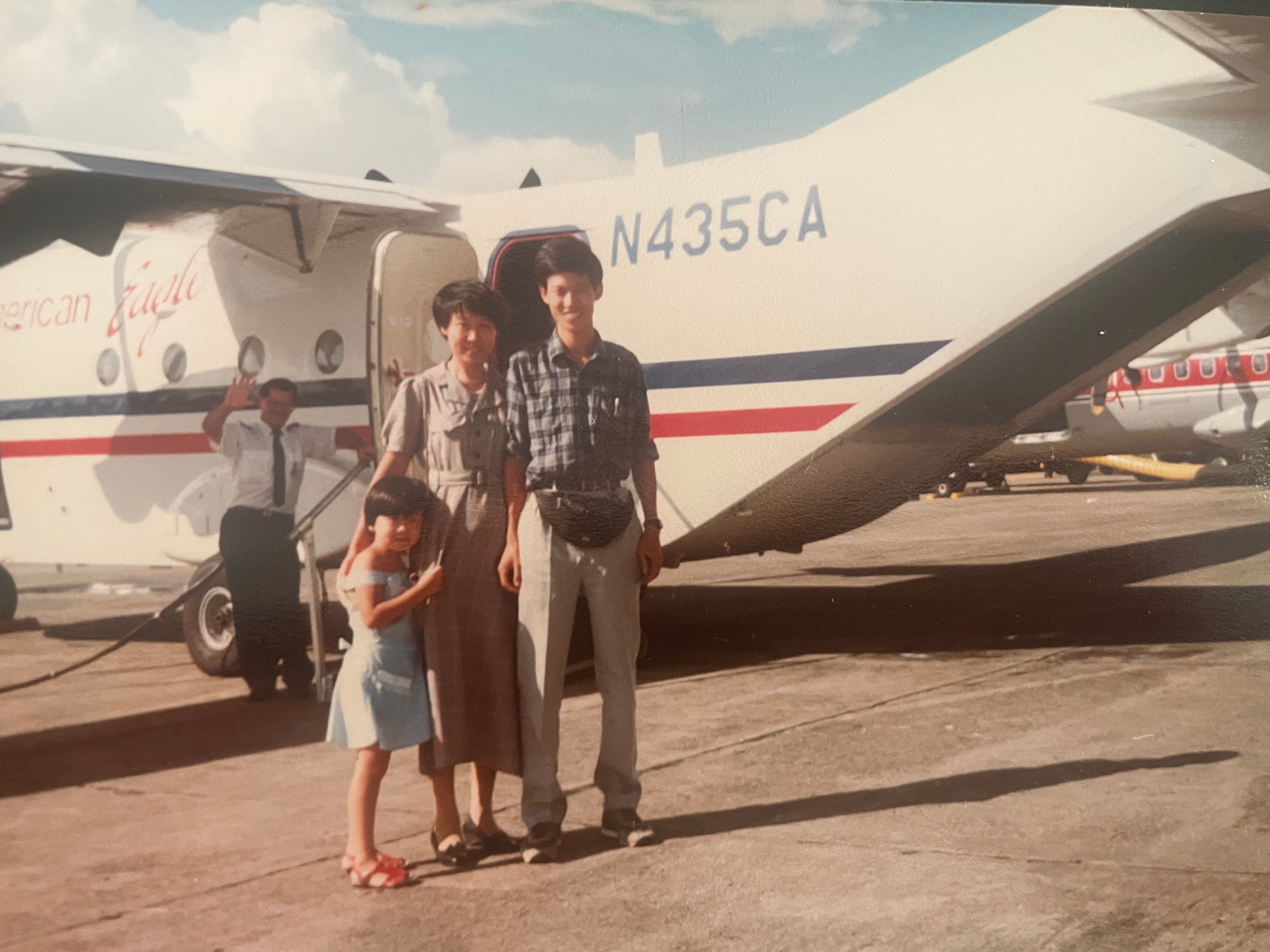 Young Christine and her parents stand in front of an airplane.
