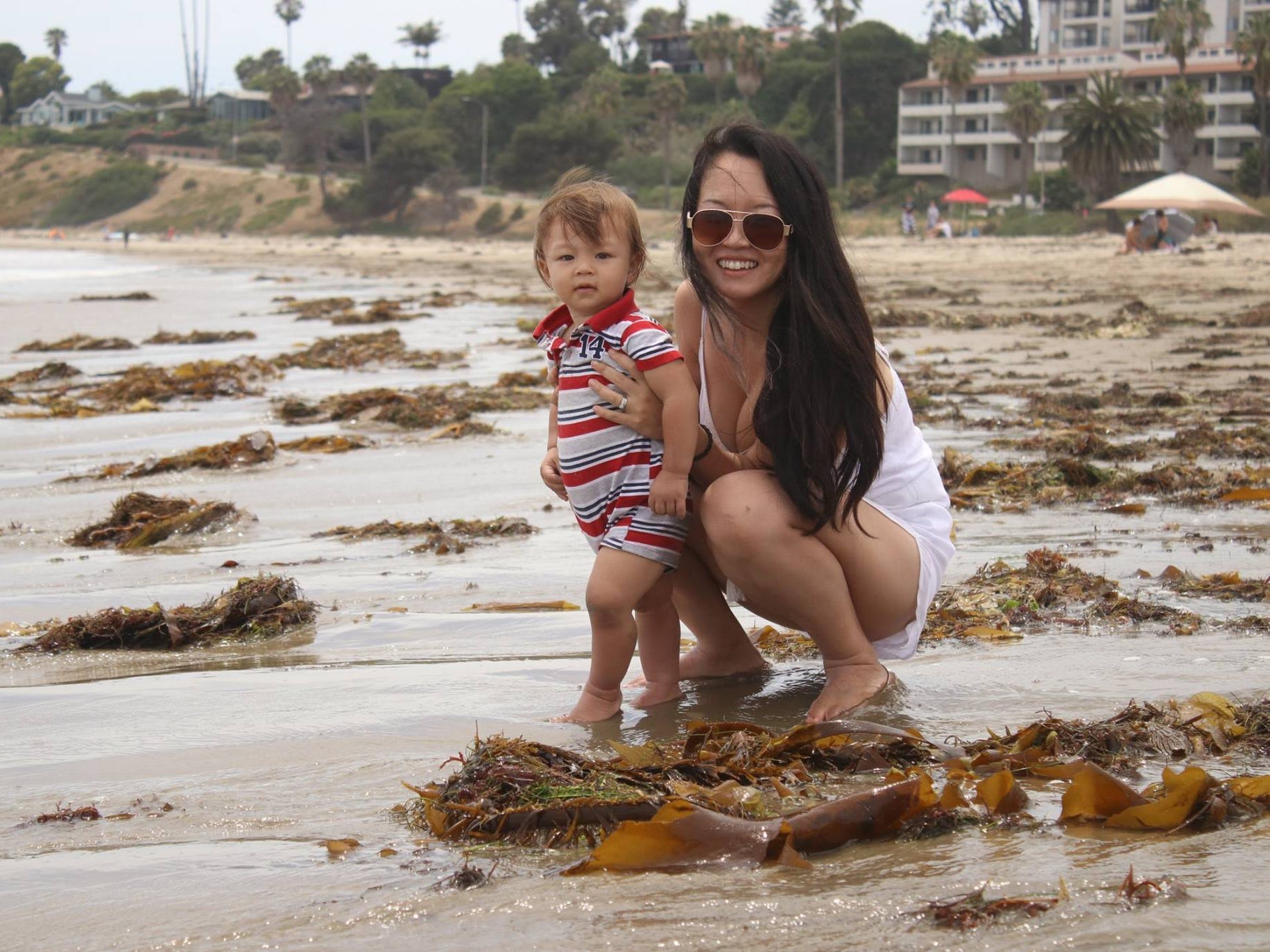 Christine squats down on the beach while holding up her young child.