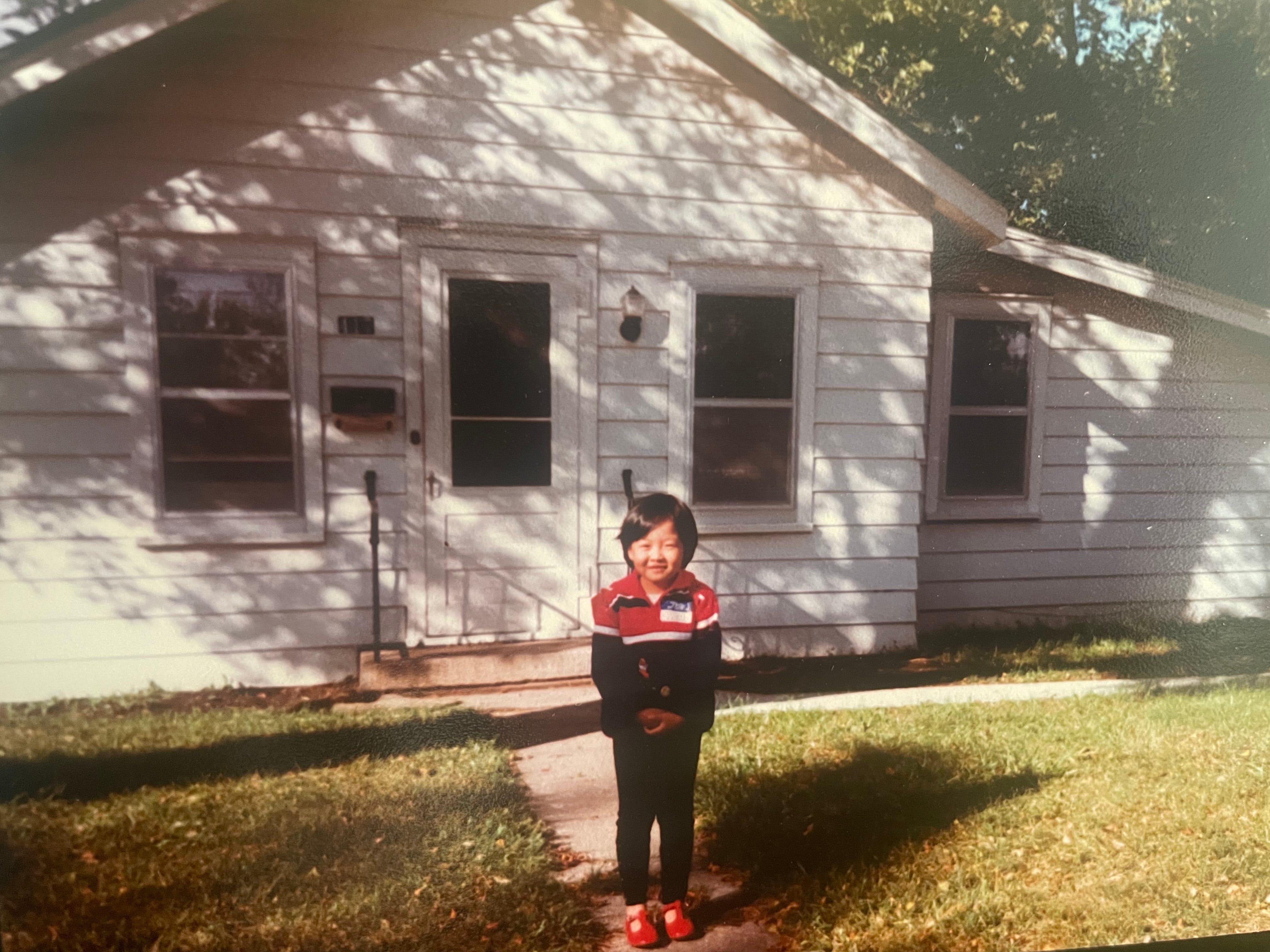 Young Christine stands in front of a suburban home.