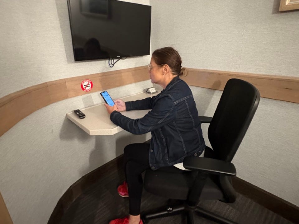 Author Jenny Powers on phone at small desk in nap room below a smart TV