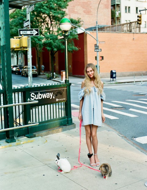Woman walking two rabbits on leashes near a subway entrance.