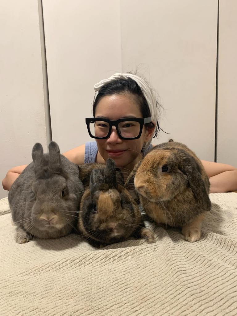 Woman with glasses cuddling three rabbits.