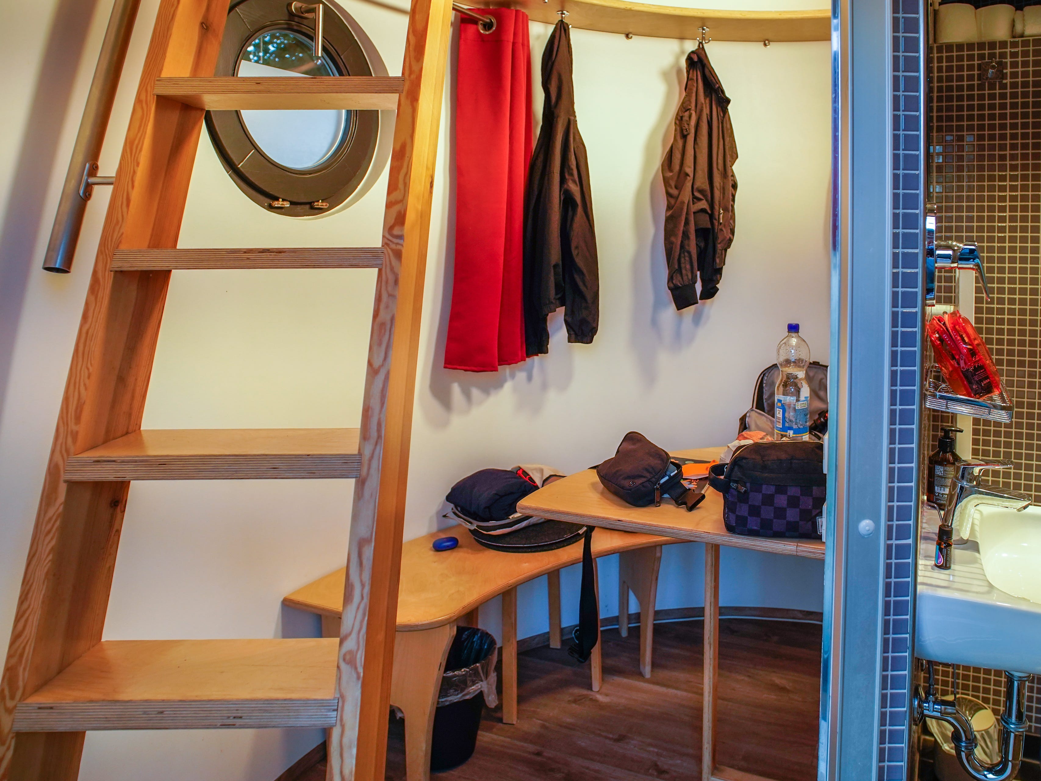 Inside a tiny home with a ladder on the left, a table in the center, and a bathroom on the right
