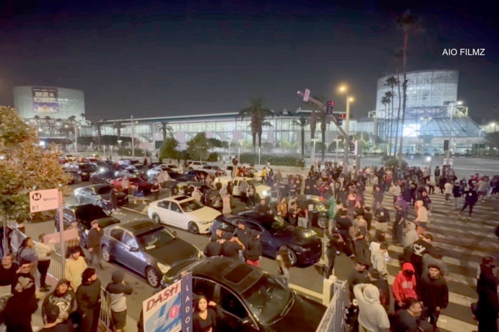 Nighttime street takeover near Crypto.com Arena in Los Angeles with over 100 vehicles.