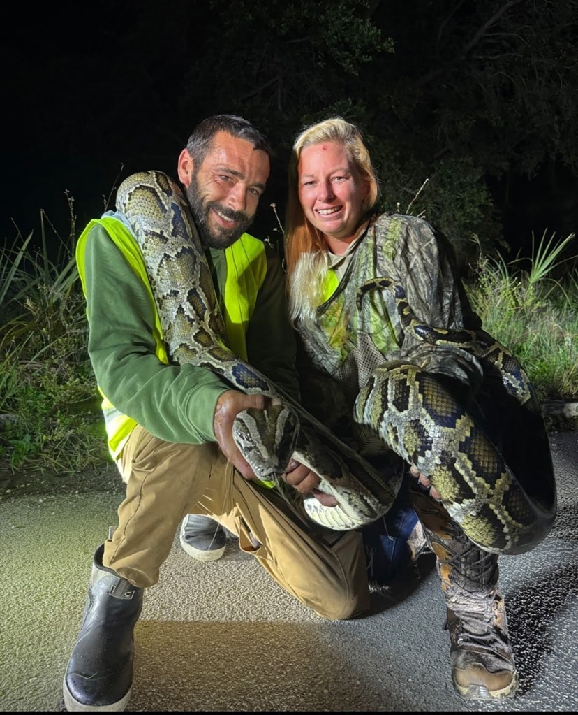 Two people holding a large Burmese python.