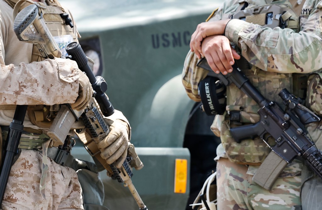 A U.S. Marine and California National Guard member stand guard with rifles.
