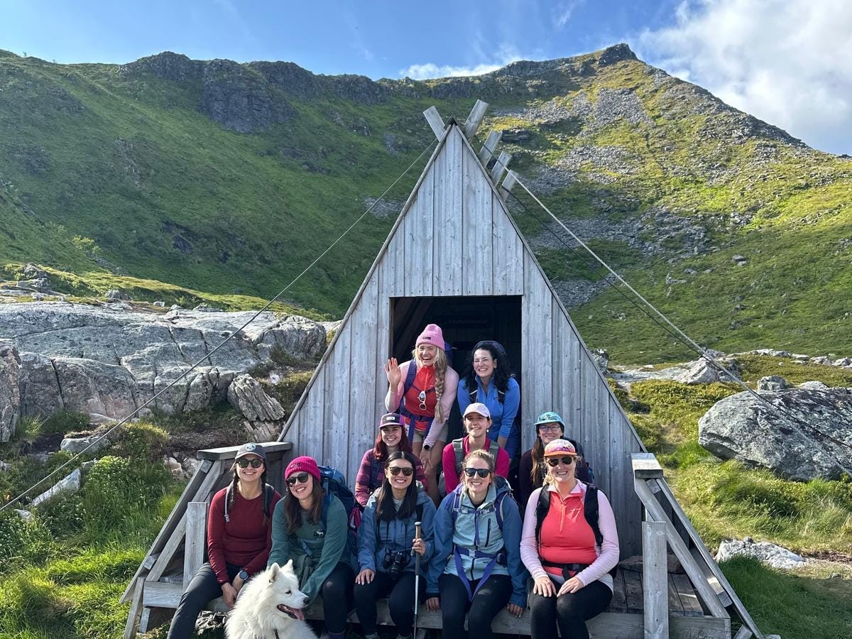 Ten women and a dog are posing on a mountain during the Arctic Dreams Retreats.