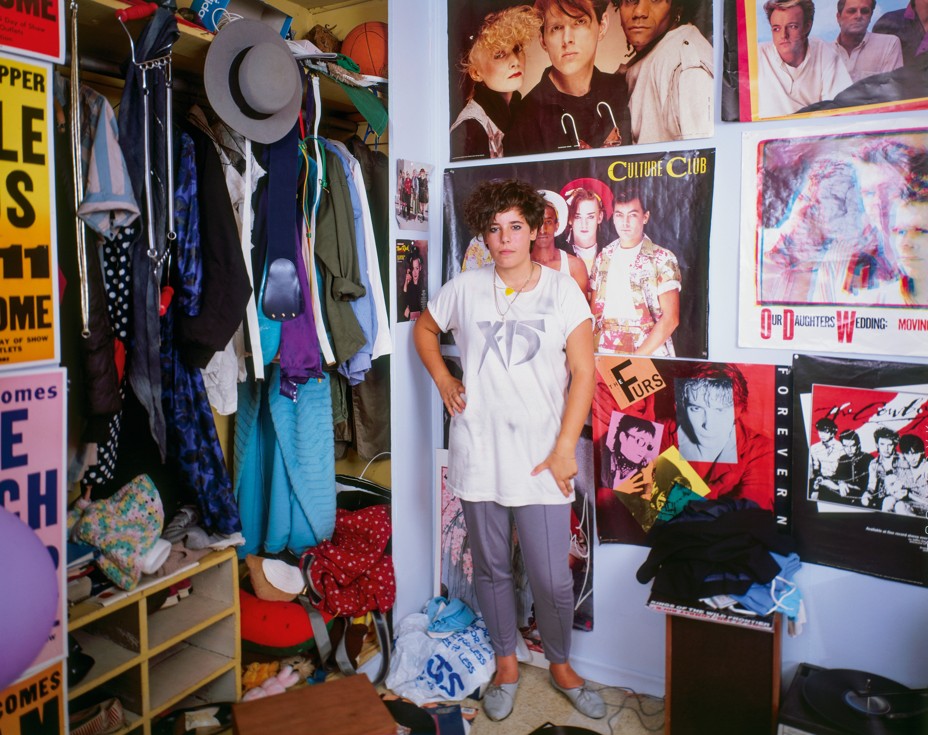 photo of girl standing next to open closet full of brightly colored clothing, with bedroom walls covered in posters including Thompson Twins, Culture Club, and the Psychedelic Furs