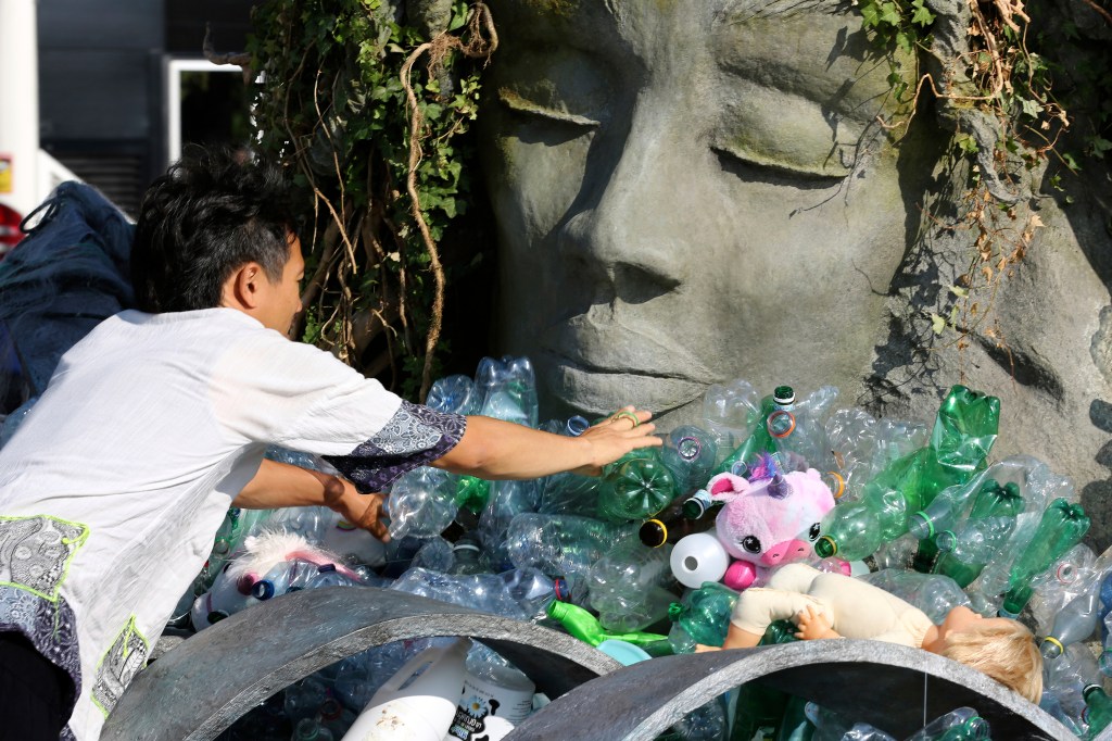 Person adding plastic bottles to a sculpture of a face at a protest.