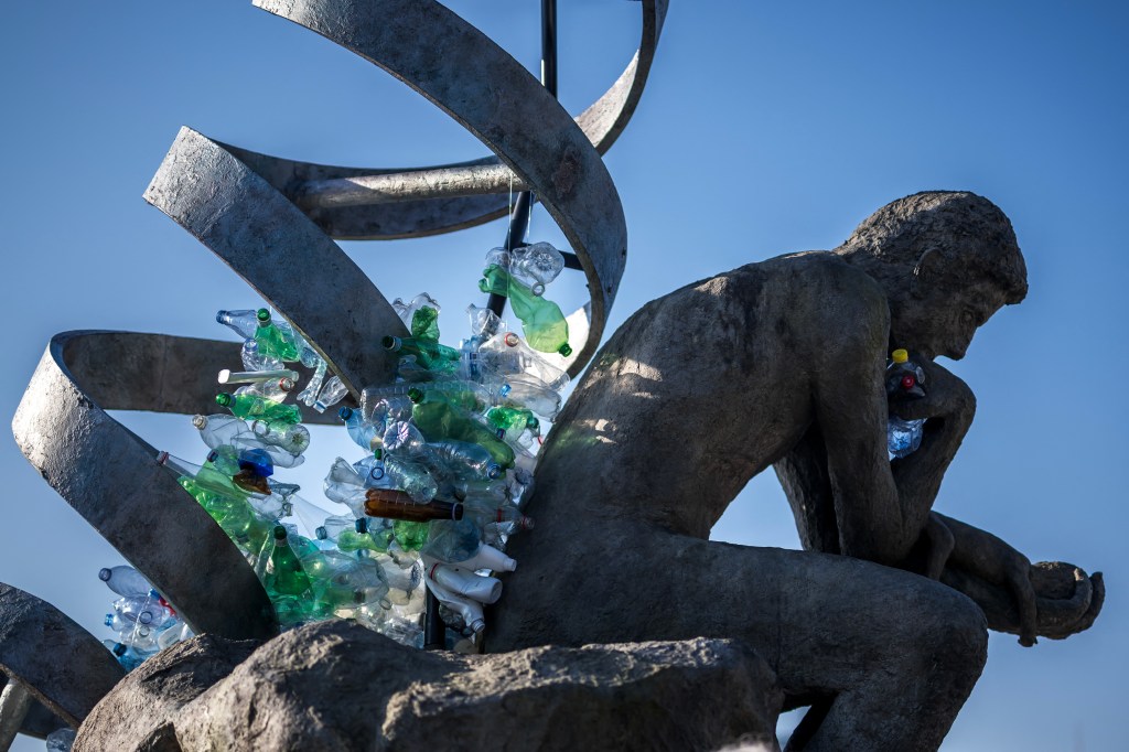 Sculpture of The Thinker burdened by plastic waste.