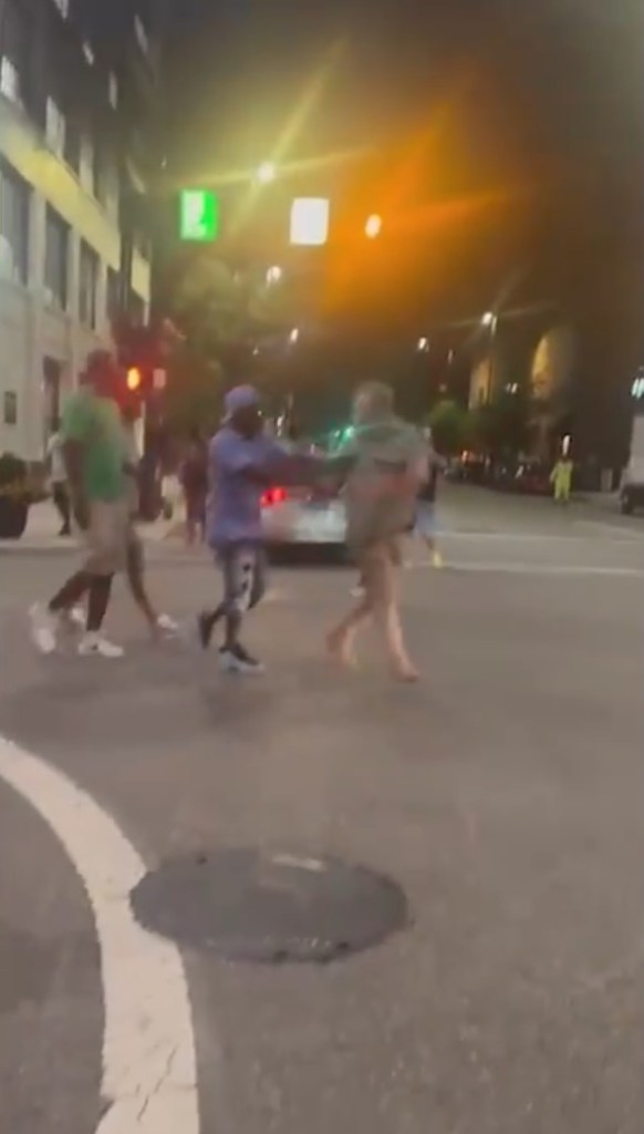 Street scene at night showing several people on a city street; some appear to be detaining another person.