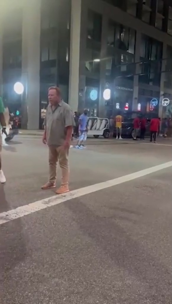 A white man standing on a city street at night, surrounded by a crowd.